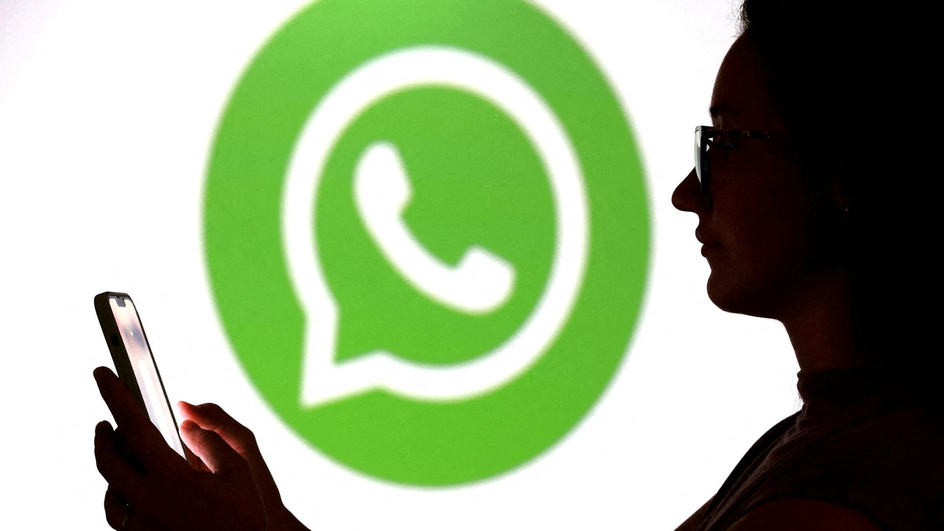 Un adolescente posa para una foto sosteniendo un teléfono inteligente frente al logotipo de WhatsApp. Foto: Reuters